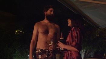 Movie still from “V/H/S Viral” (2014), directed by Aaron Moorhead – A man and a woman standing next to each other holding wine bottles; Medium shot, Over the shoulder angle