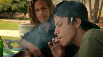 Movie still from “V/H/S Viral” (2014), directed by Aaron Moorhead – Two young men smoke cigarettes while sitting on a park bench; Close Up shot, Over the shoulder angle