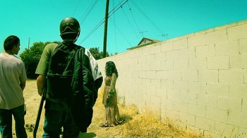 Movie still from “V/H/S Viral” (2014), directed by Aaron Moorhead – A person standing next to a brick wall near a building; Wide shot, Low angle