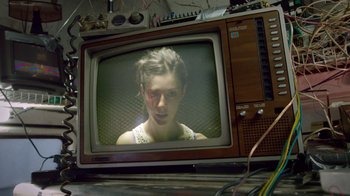 Movie still from “V/H/S Viral” (2014), directed by Aaron Moorhead – A woman is sitting in front of a television; Medium shot, Low angle