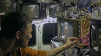 Movie still from “V/H/S Viral” (2014), directed by Aaron Moorhead – A man sitting in front of a tv in a room; Medium shot, High angle