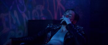 Movie still from “VFW” (2019), directed by Joe Begos – A man sitting on a couch smoking a cigarette; Medium shot, Low angle