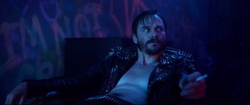 Movie still from “VFW” (2019), directed by Joe Begos – A man in a leather jacket sitting on a couch in a room; Close Up shot, High angle