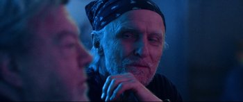 Movie still from “VFW” (2019), directed by Joe Begos – An older man with a bandanna on his head; Close Up shot, Over the shoulder angle