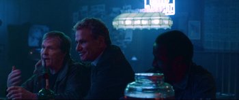 Movie still from “VFW” (2019), directed by Joe Begos – A man sitting at a table in front of a neon sign at night; Medium shot, Over the shoulder angle