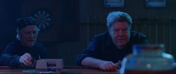 Movie still from “VFW” (2019), directed by Joe Begos – An older man sitting at a table in a dark room; Medium shot, Over the shoulder angle