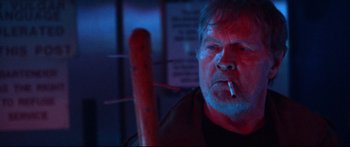 Movie still from “VFW” (2019), directed by Joe Begos – An older man smoking a cigarette while holding a hot dog; Close Up shot, Low angle