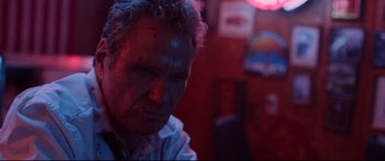 Movie still from “VFW” (2019), directed by Joe Begos – A man sitting at a table in front of a red light; Close Up shot, Low angle