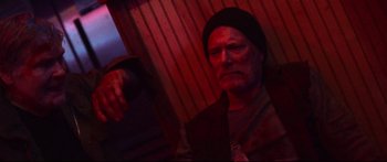 Movie still from “VFW” (2019), directed by Joe Begos – A man in a black hat is looking at the camera; Close Up shot, Overhead angle