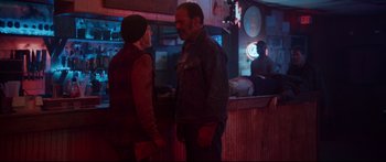 Movie still from “VFW” (2019), directed by Joe Begos – A man and a woman standing next to each other in front of a bar; Medium shot, Over the shoulder angle