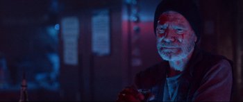 Movie still from “VFW” (2019), directed by Joe Begos – An older man is holding a glass of wine in a dark room; Close Up shot, Over the shoulder angle