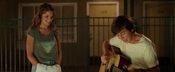 Movie still from “Vacation” (2015), directed by John Francis Daley – A young girl standing next to an older person playing a guitar; Medium shot, Over the shoulder angle