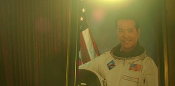 Movie still from “Another Life” (2019), created by Aaron Martin – A man in a space suit standing in front of an american flag; Medium shot, Low angle