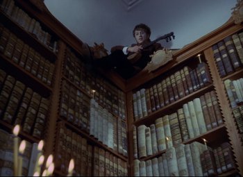 Movie still from “Valerie and Her Week of Wonders” (1970), directed by Jaromil Jires – A man sitting on top of a book shelf with a guitar; Wide shot, Overhead angle