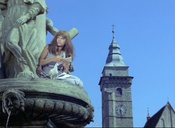 Movie still from “Valerie and Her Week of Wonders” (1970), directed by Jaromil Jires – A woman sitting on top of a statue near a clock tower; Wide shot, Low angle