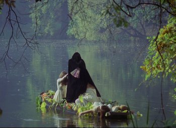 Movie still from “Valerie and Her Week of Wonders” (1970), directed by Jaromil Jires – A woman in a black dress sitting on a raft in a lake; Wide shot, High angle