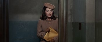 Movie still from “Valley of the Dolls” (1967), directed by Mark Robson – A woman in a brown coat and hat holding a yellow envelope; Medium shot, High angle