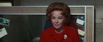 Movie still from “Valley of the Dolls” (1967), directed by Mark Robson – An older woman wearing a red coat with a white flower pin; Close Up shot, Over the shoulder angle