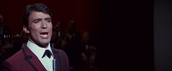 Movie still from “Valley of the Dolls” (1967), directed by Mark Robson – A man in a red jacket is in front of a group of people; Close Up shot, Over the shoulder angle