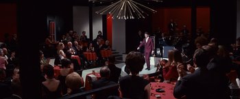 Movie still from “Valley of the Dolls” (1967), directed by Mark Robson – A man in a purple suit is on the stage; Extreme Wide shot, High angle