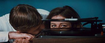 Movie still from “Valley of the Dolls” (1967), directed by Mark Robson – A man and a woman looking at each other through a hole in the wall; Close Up shot, Overhead angle