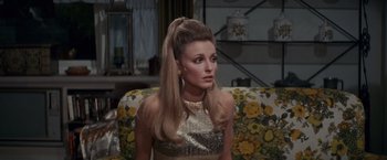 Movie still from “Valley of the Dolls” (1967), directed by Mark Robson – A woman in a gold dress sitting on a couch; Medium shot, High angle