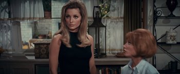Movie still from “Valley of the Dolls” (1967), directed by Mark Robson – A woman in a black dress standing in front of a lamp; Close Up shot, Over the shoulder angle