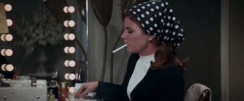 Movie still from “Valley of the Dolls” (1967), directed by Mark Robson – A woman is smoking a cigarette while sitting at a table; Medium shot, High angle