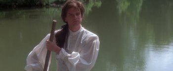 Movie still from “Valmont” (1989), directed by Milos Forman – A man in white shirt holding a stick near a body of water; Medium shot, Over the shoulder angle