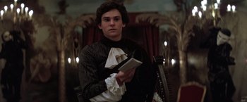 Movie still from “Valmont” (1989), directed by Milos Forman – A man in a black and white shirt holding a book in his hands; Medium shot, Low angle