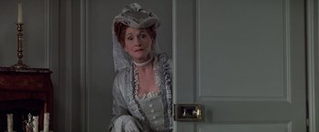 Movie still from “Valmont” (1989), directed by Milos Forman – A woman dressed in period clothing sitting in a doorway; Medium shot, Over the shoulder angle