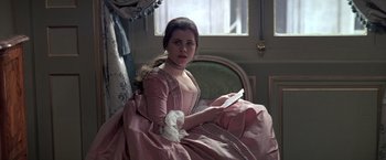 Movie still from “Valmont” (1989), directed by Milos Forman – A woman in a pink dress sitting on a couch; Medium shot, Over the shoulder angle