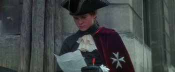 Movie still from “Valmont” (1989), directed by Milos Forman – A man in a pirate costume reading a paper; Medium shot, Over the shoulder angle