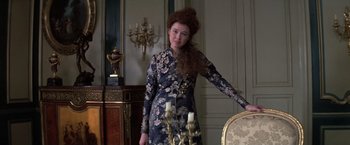 Movie still from “Valmont” (1989), directed by Milos Forman – A woman in a dress standing next to a chair; Medium shot, Over the shoulder angle