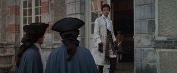 Movie still from “Valmont” (1989), directed by Milos Forman – A man dressed in period clothing standing in front of a building; Medium shot, Over the shoulder angle