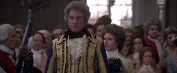 Movie still from “Valmont” (1989), directed by Milos Forman – A man dressed in a suit and wig standing in front of a group of people; Medium shot, Low angle