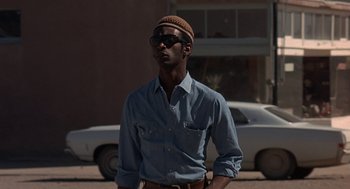 Movie still from “Vanishing Point” (1971), directed by Richard C. Sarafian – A man wearing a hat and sunglasses standing in front of a white car; Medium shot, Low angle
