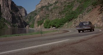 Movie still from “Vanishing Point” (1971), directed by Richard C. Sarafian – A car driving down a road next to a body of water; Extreme Wide shot, High angle