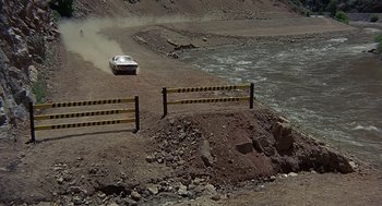 Movie still from “Vanishing Point” (1971), directed by Richard C. Sarafian – A car driving down a dirt road next to a body of water; Extreme Wide shot, High angle