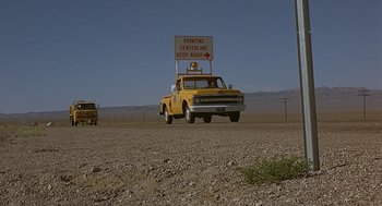 Movie still from “Vanishing Point” (1971), directed by Richard C. Sarafian – A yellow truck with a sign on the back of it; Extreme Wide shot, Low angle