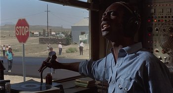 Movie still from “Vanishing Point” (1971), directed by Richard C. Sarafian – A man with a microphone and headphones is singing; Close Up shot, Low angle