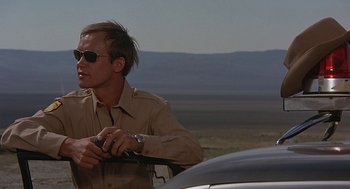 Movie still from “Vanishing Point” (1971), directed by Richard C. Sarafian – A man in a tan shirt and sunglasses holding a car key; Close Up shot, Low angle