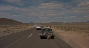 Movie still from “Vanishing Point” (1971), directed by Richard C. Sarafian – Two cars driving down a road near some mountains; Extreme Wide shot, High angle
