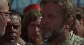 Movie still from “Vanishing Point” (1971), directed by Richard C. Sarafian – A man with long hair and a beard talking to a crowd of onlookers; Close Up shot, Over the shoulder angle