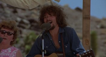 Movie still from “Vanishing Point” (1971), directed by Richard C. Sarafian – A man with long hair is playing an instrument; Close Up shot, Low angle