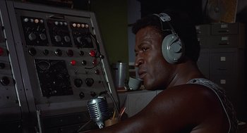 Movie still from “Vanishing Point” (1971), directed by Richard C. Sarafian – A man wearing headphones and holding a microphone in front of a control panel; Close Up shot, Low angle