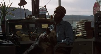 Movie still from “Vanishing Point” (1971), directed by Richard C. Sarafian – A man sitting in a chair with a dog; Medium shot, Over the shoulder angle