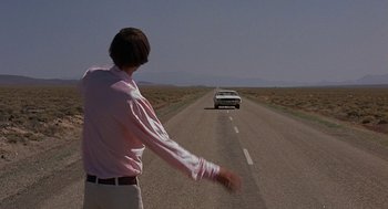 Movie still from “Vanishing Point” (1971), directed by Richard C. Sarafian – A man standing on the side of a road next to a car; Wide shot, Over the shoulder angle