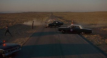 Movie still from “Vanishing Point” (1971), directed by Richard C. Sarafian – Two police cars parked on the side of a road; Extreme Wide shot, High angle