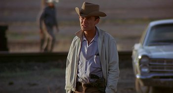 Movie still from “Vanishing Point” (1971), directed by Richard C. Sarafian – A man wearing a cowboy hat standing on top of a field; Medium shot, Over the shoulder angle
